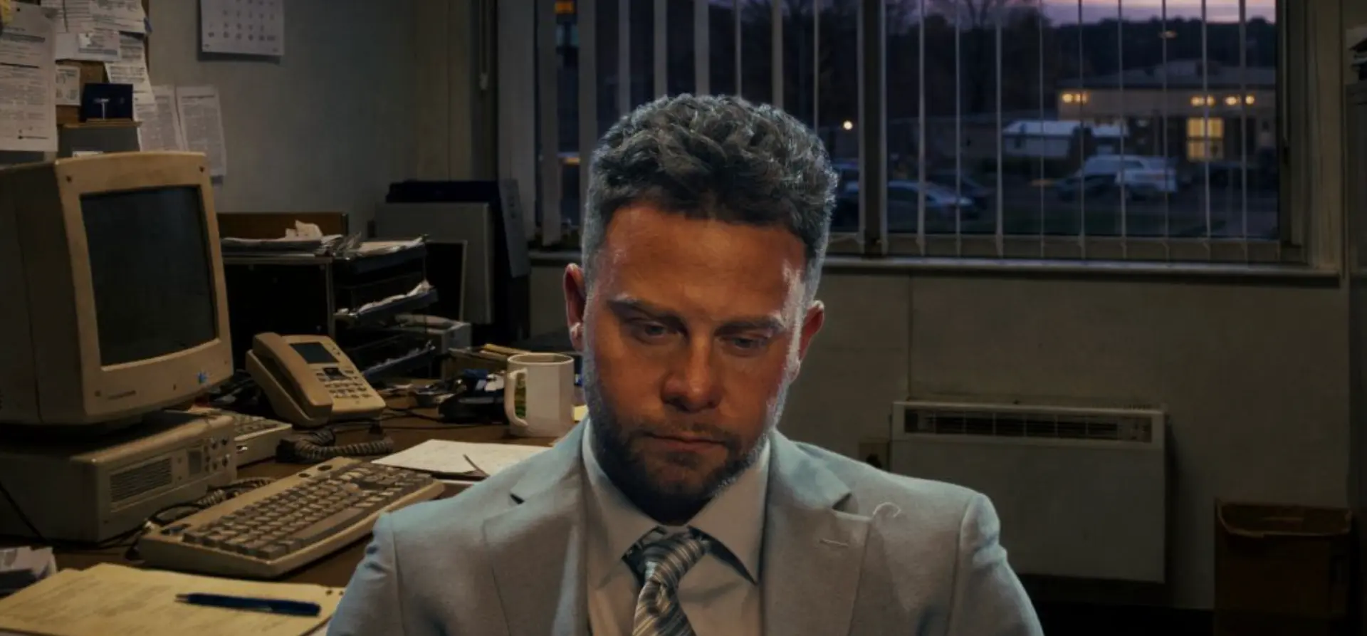 In-game scene: the boss at a cluttered office desk at dusk